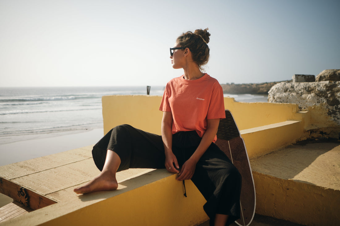 Frau mit einem NIKN Shirt mit dreamer Embroidery sitzt still am Meer und blick in die Weite.