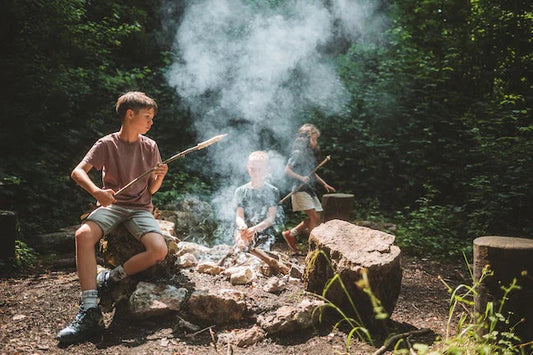 Drei Kinder sind im Wald am Schlangenbrot grillieren über einem Feuer.